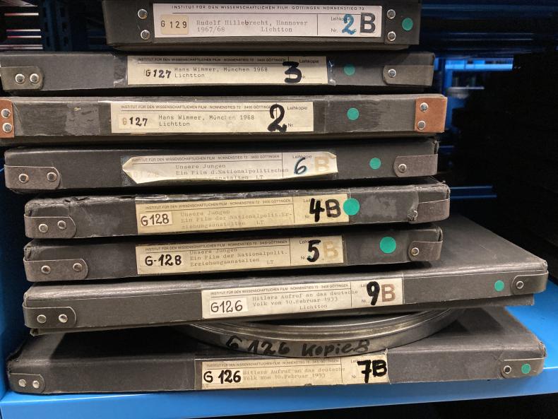 A stack of IWF-Film prints from the series Filmdokumente zur Zeitgeschichte at the TIB Hannover, Rethen Archive. The handwritten number on the right hand side indicates the number of each film copy. The higher the number, the more the film had been borrowed and hence a new copy had to be ordered.